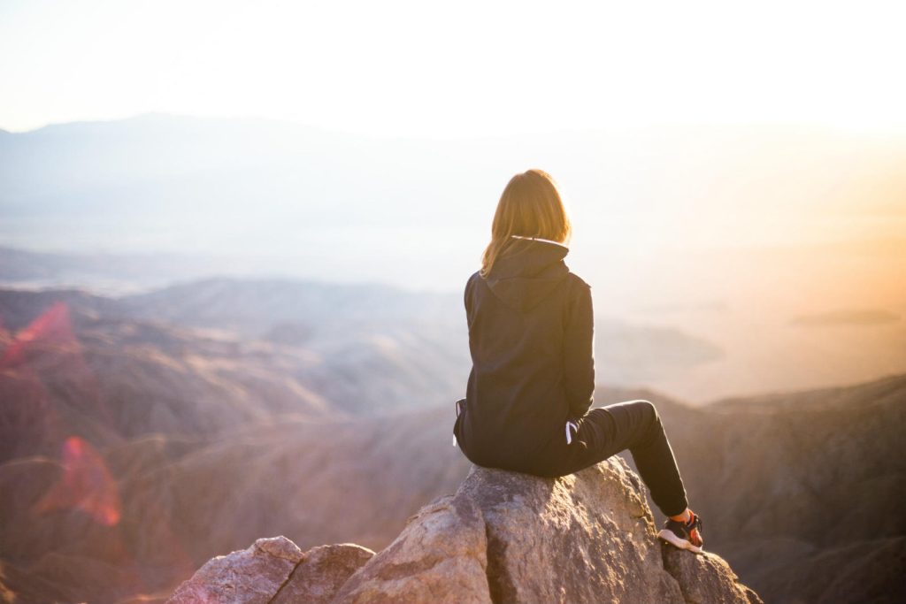 Woman sitting on top of a mountain watching the sun rise