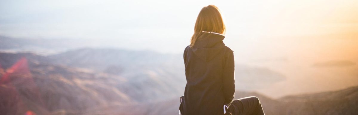 Woman sitting on top of a mountain watching the sun rise