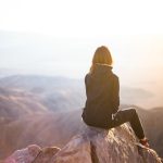 Woman sitting on top of a mountain watching the sun rise