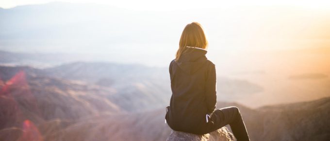 Woman sitting on top of a mountain watching the sun rise