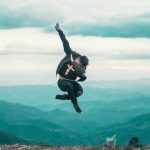 man jumping up in the air with mountains and sky in the background