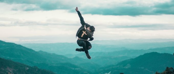 man jumping up in the air with mountains and sky in the background